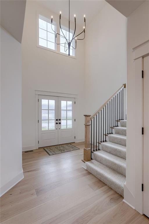 entryway with french doors, light hardwood / wood-style floors, a high ceiling, and an inviting chandelier