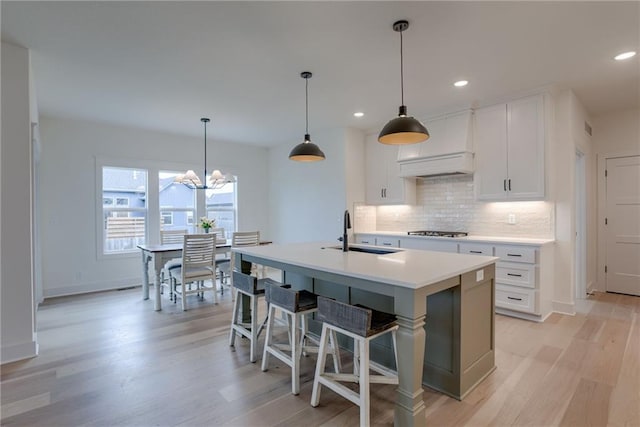 kitchen featuring sink, decorative light fixtures, a center island with sink, decorative backsplash, and white cabinets