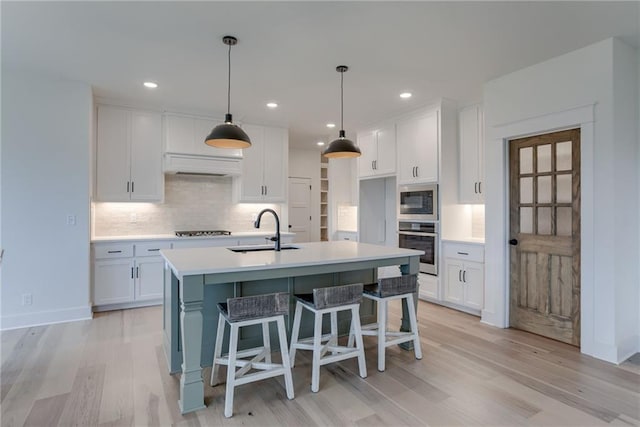 kitchen featuring sink, a kitchen island with sink, white cabinetry, built in microwave, and oven