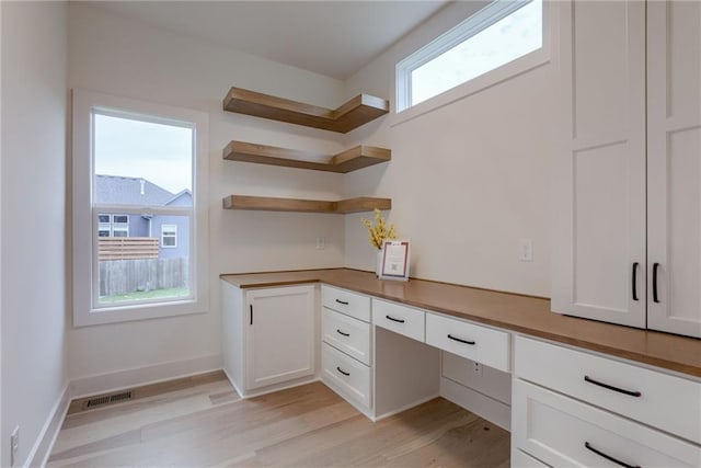 kitchen with built in desk, white cabinets, and light hardwood / wood-style floors