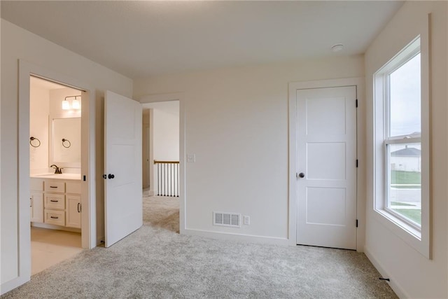 unfurnished bedroom with ensuite bathroom, sink, and light carpet