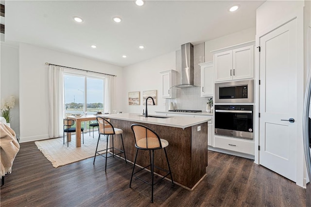 kitchen featuring wall chimney range hood, stainless steel appliances, sink, white cabinets, and dark hardwood / wood-style flooring