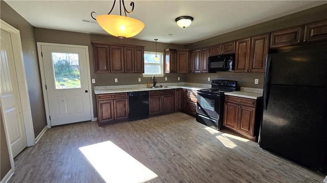 kitchen featuring light wood-type flooring, black appliances, sink, and decorative light fixtures