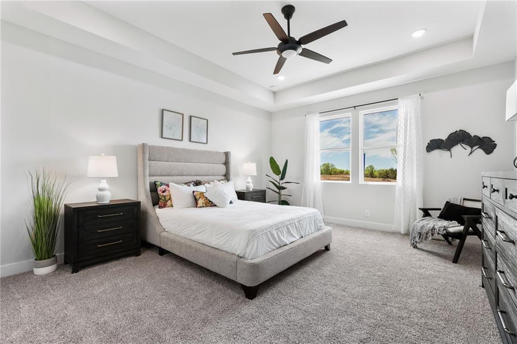 carpeted bedroom featuring ceiling fan and a tray ceiling