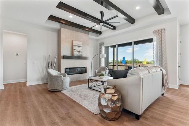 living room with beam ceiling, light hardwood / wood-style flooring, a tile fireplace, and ceiling fan