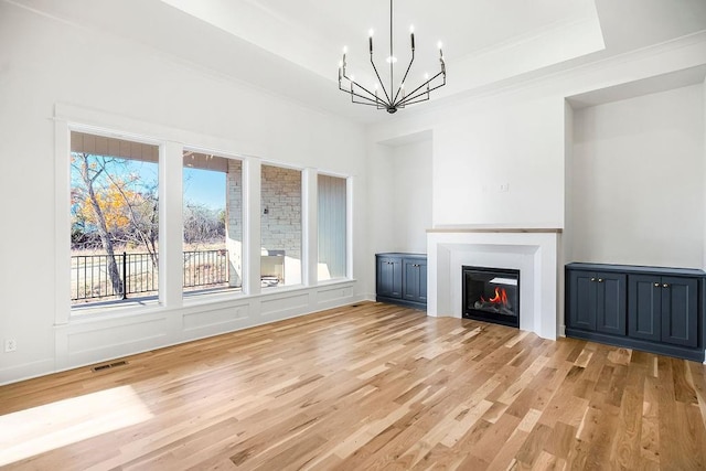 unfurnished living room featuring light wood-type flooring, a tray ceiling, plenty of natural light, and a notable chandelier