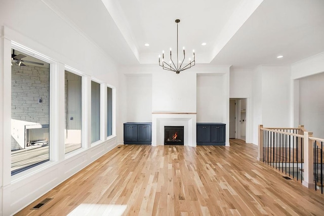 unfurnished living room featuring ceiling fan with notable chandelier, light wood-type flooring, and a raised ceiling