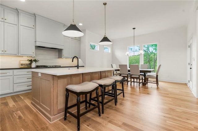 12484 S Barth Rd, Olathe, KS 66061 - kitchen featuring backsplash, recessed lighting, light wood-style flooring, a kitchen island with sink, and a breakfast bar