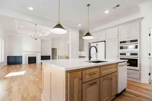 12484 S Barth Rd, Olathe, KS 66061 - kitchen with white appliances, light wood-type flooring, light countertops, a center island with sink, and hanging light fixtures
