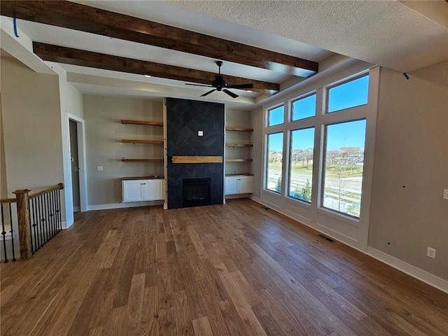 unfurnished living room with built in features, ceiling fan, dark hardwood / wood-style floors, a fireplace, and a textured ceiling