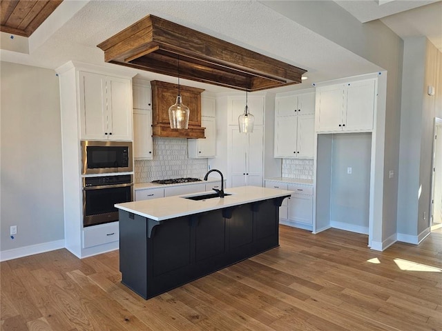 kitchen with sink, hanging light fixtures, stainless steel appliances, white cabinets, and a center island with sink