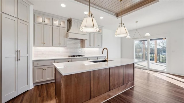 kitchen featuring pendant lighting, a center island with sink, sink, decorative backsplash, and gas stovetop