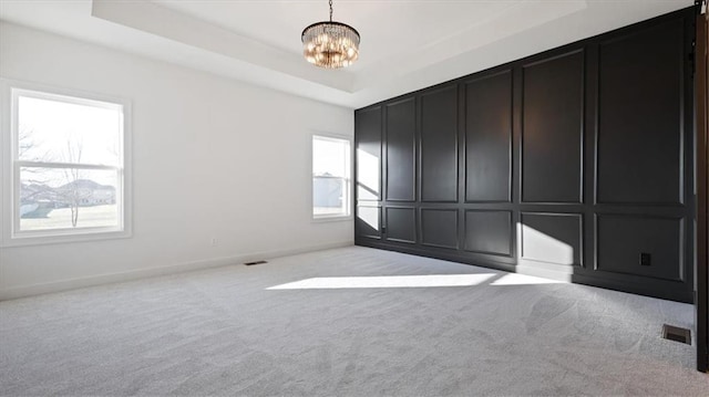 carpeted empty room with a raised ceiling and an inviting chandelier