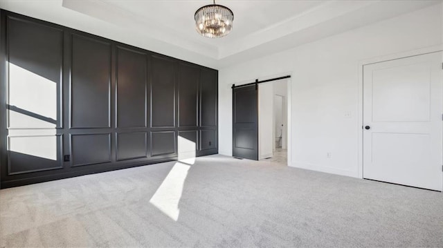 unfurnished bedroom featuring a raised ceiling, a barn door, light colored carpet, and an inviting chandelier