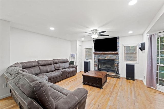 living room with a stone fireplace, light wood-type flooring, and ceiling fan