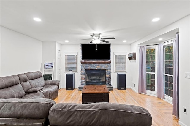 living room featuring a stone fireplace, light hardwood / wood-style floors, and ceiling fan