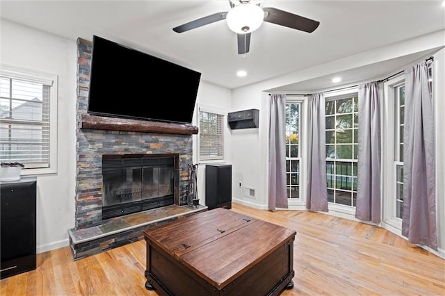 living room with a fireplace, ceiling fan, and light wood-type flooring