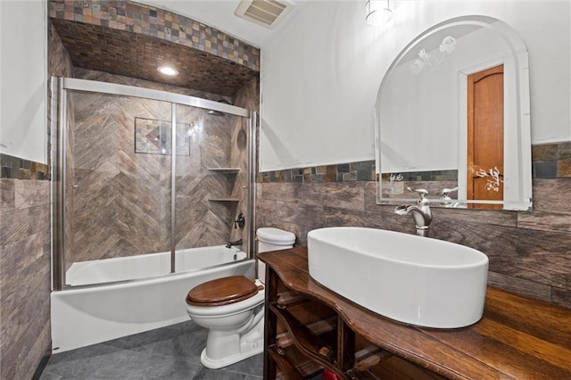 full bathroom featuring toilet, vanity, shower / bath combination with glass door, and tile walls