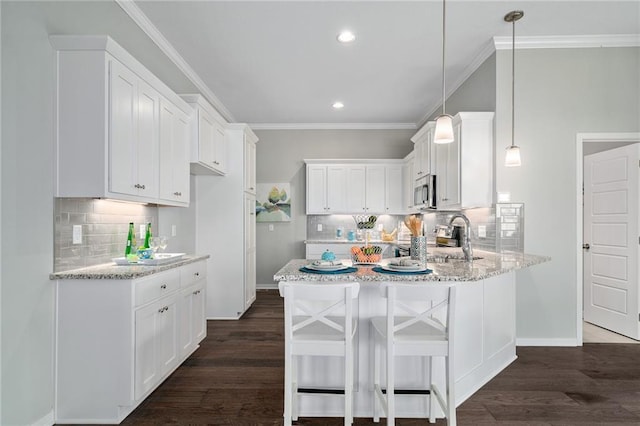 kitchen with crown molding, a breakfast bar, white cabinetry, hanging light fixtures, and light stone counters