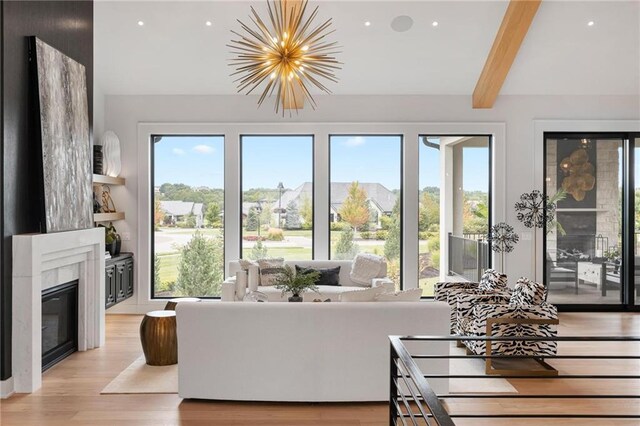 living room with beamed ceiling, light wood-type flooring, a high end fireplace, and a chandelier