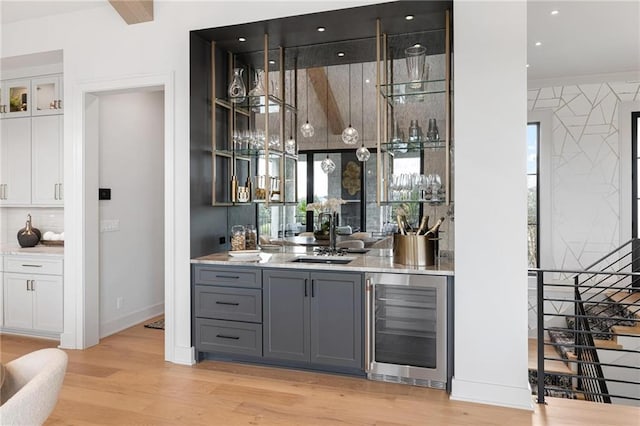 bar with light wood-style floors, a sink, wet bar, beverage cooler, and baseboards