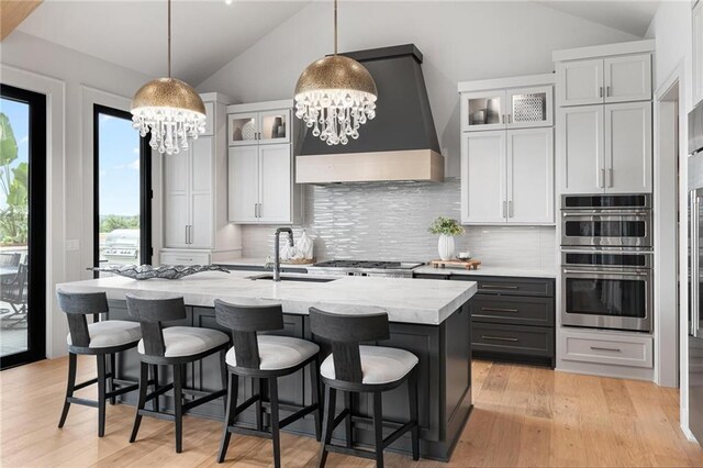 kitchen with decorative backsplash, stainless steel double oven, custom range hood, a notable chandelier, and vaulted ceiling