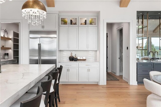 kitchen with pendant lighting, decorative backsplash, built in fridge, white cabinetry, and light hardwood / wood-style flooring