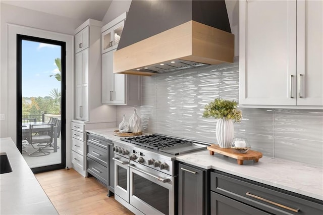 kitchen with light stone counters, light wood finished floors, custom range hood, backsplash, and double oven range