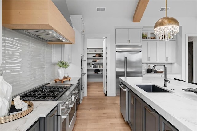 kitchen with premium range hood, sink, tasteful backsplash, white cabinetry, and light hardwood / wood-style flooring