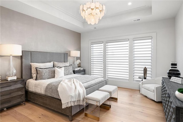 bedroom with light wood-type flooring, a tray ceiling, a chandelier, and visible vents