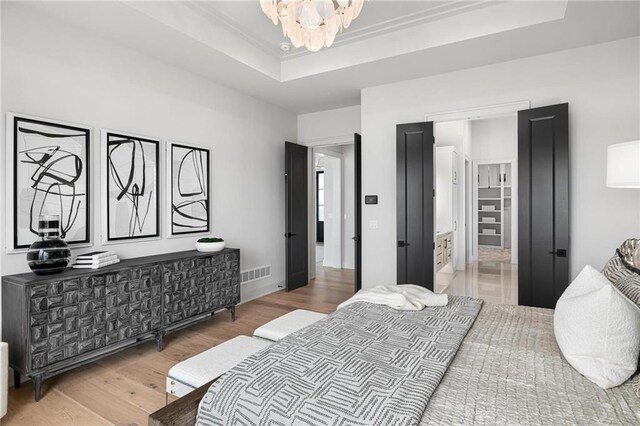 bedroom featuring connected bathroom, an inviting chandelier, hardwood / wood-style flooring, and a raised ceiling