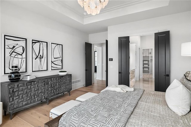 bedroom featuring a chandelier, a tray ceiling, wood finished floors, and visible vents