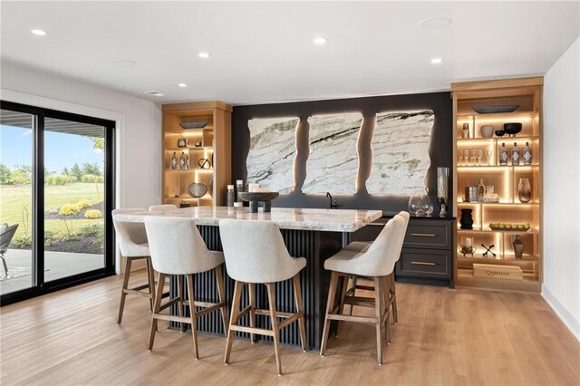 bar featuring built in shelves, light stone counters, and light hardwood / wood-style floors