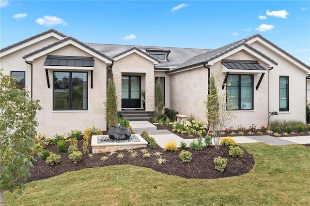 modern farmhouse featuring stone siding, a standing seam roof, a front yard, and a tiled roof