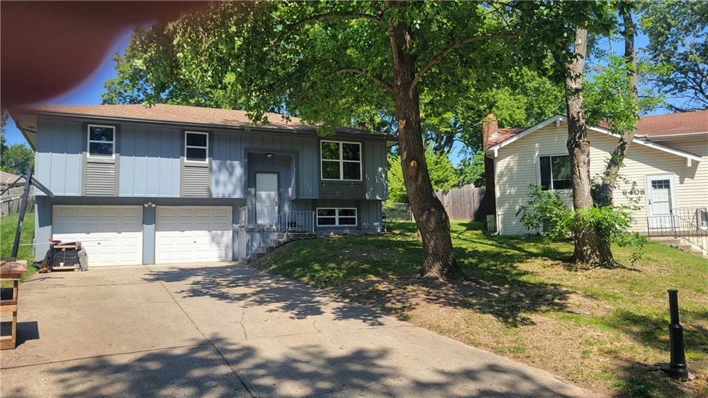 split foyer home with board and batten siding, fence, a garage, driveway, and a front lawn