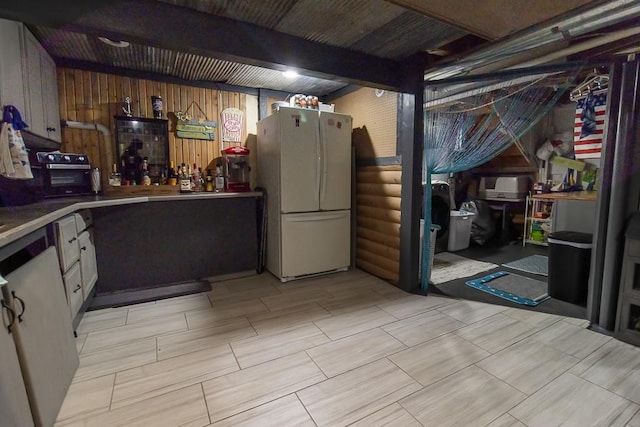 basement featuring white refrigerator and wood walls