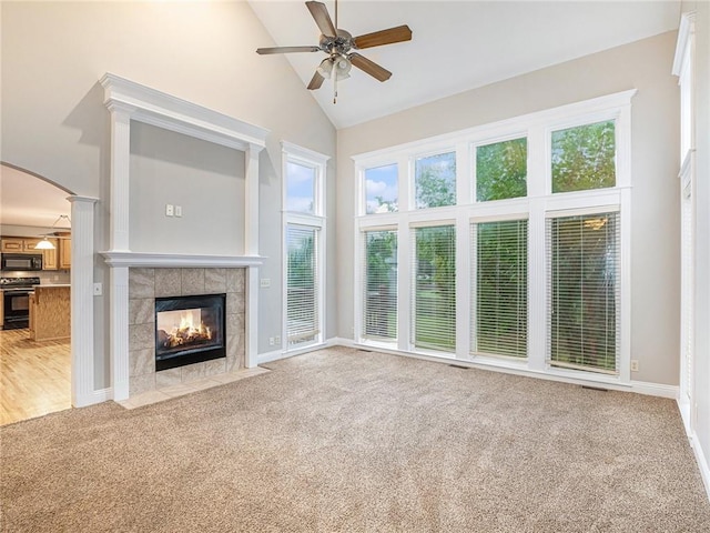 unfurnished living room featuring arched walkways, high vaulted ceiling, ceiling fan, light colored carpet, and a fireplace