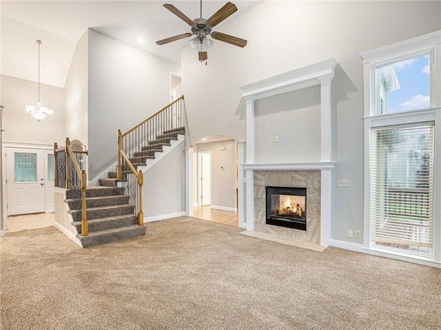 unfurnished living room featuring stairway, a tiled fireplace, carpet flooring, and a towering ceiling