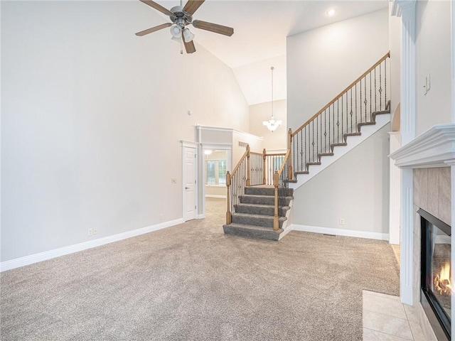 unfurnished living room with baseboards, a tiled fireplace, light colored carpet, stairway, and high vaulted ceiling