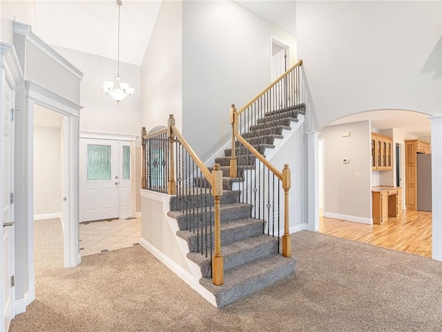 carpeted foyer with arched walkways, a high ceiling, an inviting chandelier, baseboards, and stairs