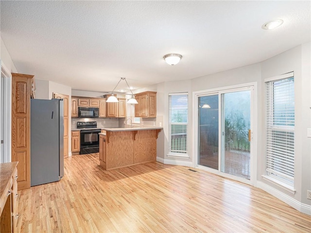 kitchen with a breakfast bar area, light countertops, light wood-type flooring, a peninsula, and black appliances