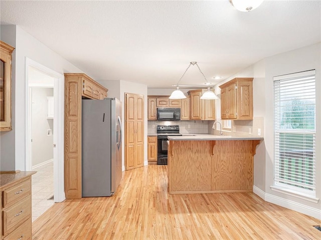 kitchen with tasteful backsplash, a kitchen breakfast bar, a peninsula, black appliances, and a sink