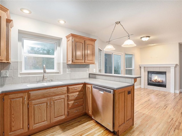 kitchen featuring tasteful backsplash, stainless steel dishwasher, light wood-style floors, a sink, and a peninsula