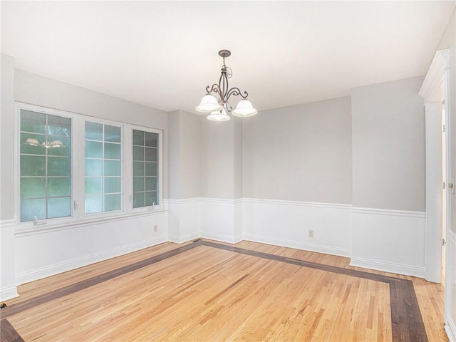 unfurnished room with a chandelier, light wood-style flooring, and baseboards