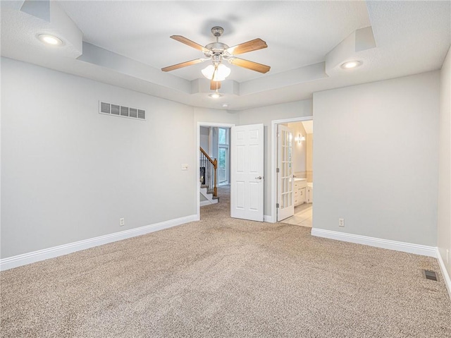 spare room featuring a raised ceiling, visible vents, light carpet, and baseboards