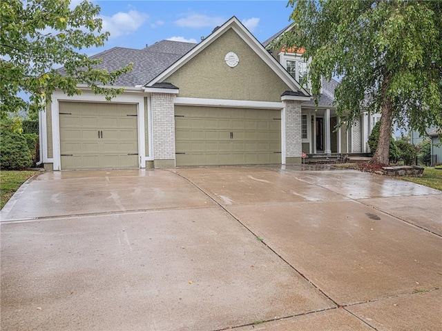 view of front of house with brick siding, stucco siding, a shingled roof, an attached garage, and driveway