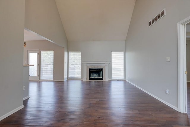 unfurnished living room featuring visible vents, dark wood-type flooring, a glass covered fireplace, high vaulted ceiling, and baseboards