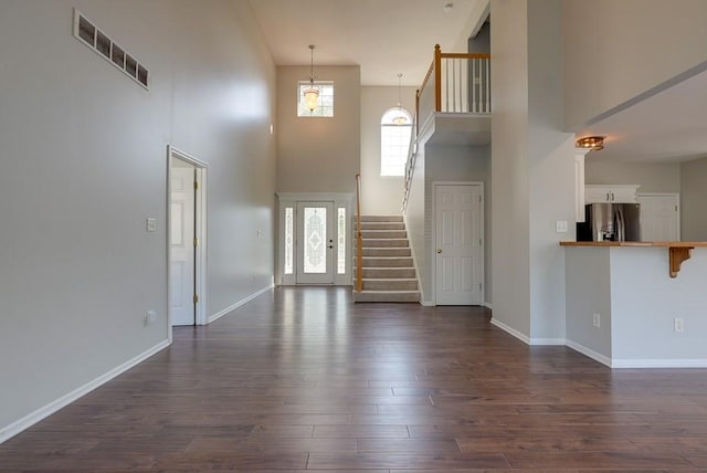 unfurnished living room featuring dark wood finished floors, visible vents, a towering ceiling, baseboards, and stairs