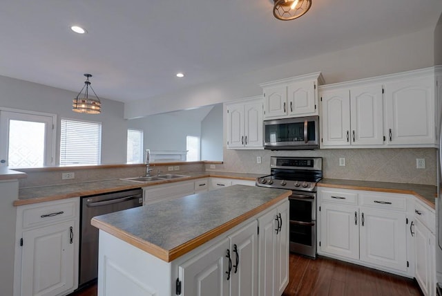 kitchen with decorative light fixtures, appliances with stainless steel finishes, white cabinets, a kitchen island, and a sink