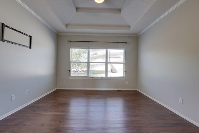 empty room featuring dark wood-style floors, a tray ceiling, ornamental molding, and baseboards